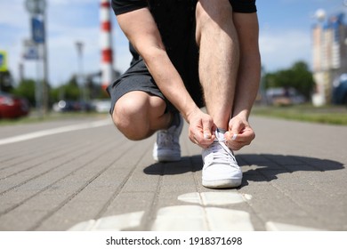 Close-up of man tying shoelaces on white sneakers. Male person squatting on sidewalk. Sunny morning or day. Male going on footpath. Sport and healthy lifestyle concept - Powered by Shutterstock