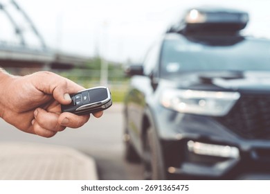 Close-up of a man unlocking a car using a key fob, with a black car parked in a car park in the background