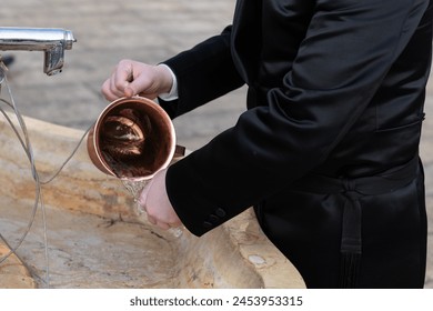 Closeup of a man using a copper natla or Jewish ritual hand washing cup to ritually wash his hands before prayer at the Western Wall in Jerusalem, Israel.   - Powered by Shutterstock