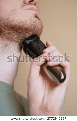 Closeup of a man using an electric shaver to trim facial hair. The image shows the focus on personal grooming and maintaining a neat beard appearance using a black electric razor.