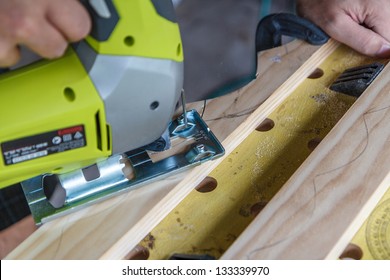 Close-up Of A Man Using A Jigsaw On A Piece Of Wood. The Jigsaw Is Carving Out Semi-circles To Make A Wine Rack.