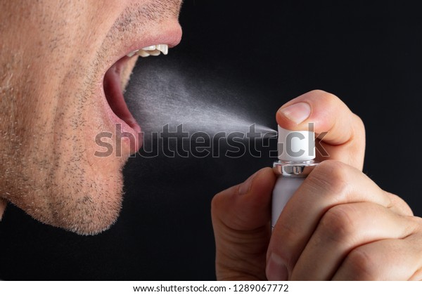 Close-up Of Man Using Mouth Freshener Against\
Black Background