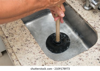 A closeup of the man using a plunger to unstop the kitchen sink 