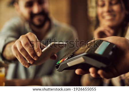 Close-up of man using smart phone while making contactless payment in a cafe. 