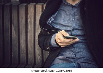 closeup of man using smartphone, casual male person sitting on bench is typing on mobile phone