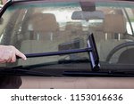 Close-up of man using squeegee to clean the windshield of a car with a GPS visable inside on dash