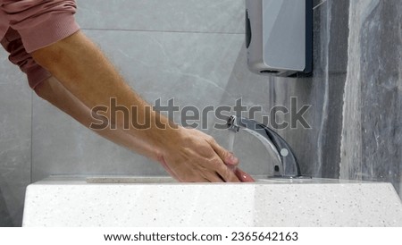 Close-up of a man washing his hands using a touchless faucet in a restroom