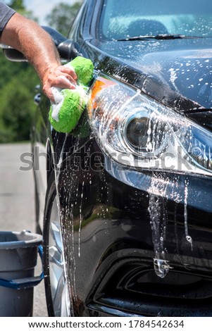 Closeup man washing new black sedan family car with sponge, soap, suds, sunny summer day, pampering car, automobile maintenance, shiny, sparkling, wheels, tires, foam, wheels, tires, bucket