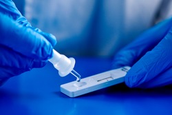 Closeup Of A Man, Wearing Blue Surgical Gloves, Placing The Sample Into The Covid-19 Antigen Diagnostic Test Device, On A Blue Surface