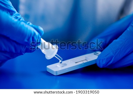 closeup of a man, wearing blue surgical gloves, placing the sample into the covid-19 antigen diagnostic test device, on a blue surface