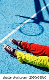 closeup of a man, wearing a colorful clown costume, lying face up on an outdoor basketball court