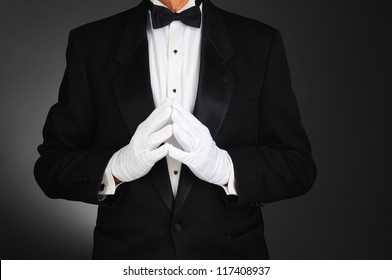 Closeup of a man wearing a tuxedo with his hands together in front of his torso. Man is unrecognizable. Horizontal format on a light to dark gray background.