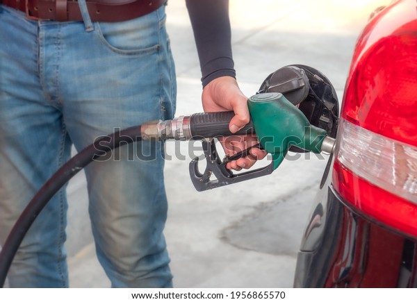 Closeup of man wears jean holding\
green fuel pump nozzle filling gasoline into black car at gas\
station.  Self-service vehicle refuelling offer economy\
price.