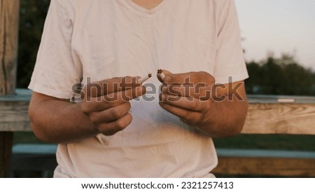 A closeup of the man in a white t-shirt holding two pieces of cigarette. Stop smoking concept.