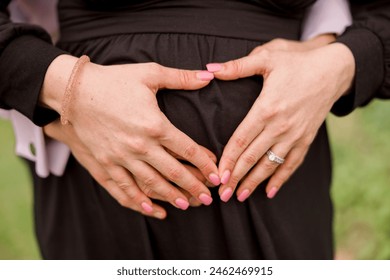 Close-up of a man and woman's hands as they make a heart shape over her pregnancy belly - Powered by Shutterstock