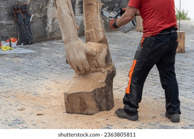 Close-up of a man in work clothes making a sculpture of a hand and a wooden arm carving a log with a chainsaw.
