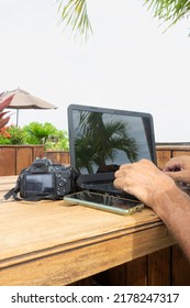 Close-up Of A Man Working On A White-screen Laptop Computer On Old Wooden Table Outside.