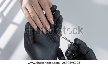 Close-up of manicure master applying light beige gel polish to elegant almond-shaped nails in salon
