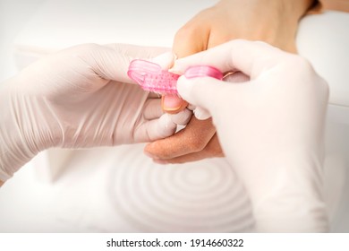 Nahaufnahme eines Manikuristen besteht darin, in einem Nagelsalon Staub mit einer rosa Plastikbürste aus weiblichen Fingernägeln in einer Nagelspritze zu brennen.