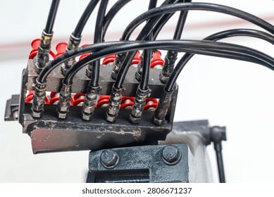Close-up of a manifold block with multiple black hydraulic high-pressure hoses connected to industrial machinery components.