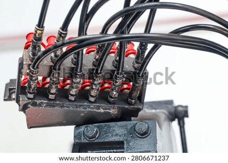 Close-up of a manifold block with multiple black hydraulic high-pressure hoses connected to industrial machinery components.