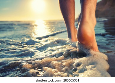 Closeup of a man's bare feet walking at a beach at sunset, with a wave's edge foaming gently beneath them, toned colors - Shutterstock ID 285605351
