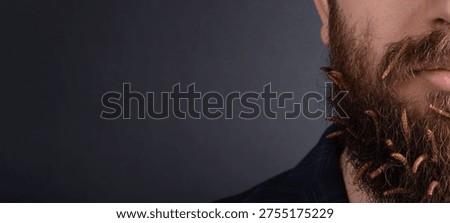 Close-up of a man's beard with live worms crawling through facial hair against a dark background, concept for shock or unique grooming.