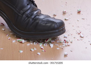 Closeup Man's Black Dress Shoe Stepping Onto And Shattering Christmas Candy Cane On Wood Floor