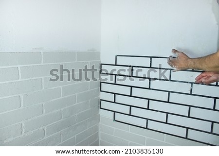 Close-up - a man's hand applies a stencil to the wall to make a brick wall. House renovation, decorative plaster on the wall for a brick. Interior decoration