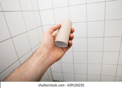 Close-up Of A Man's Hand Holding Empty Toilet Paper Roll In Bathroom