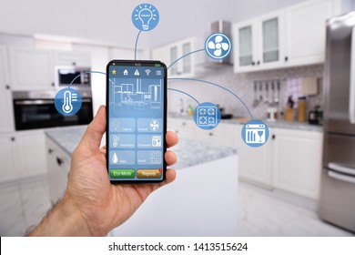 Close-up Of Man's Hand Holding Mobile With Smart Home Control Icon Feature With Kitchen Background
