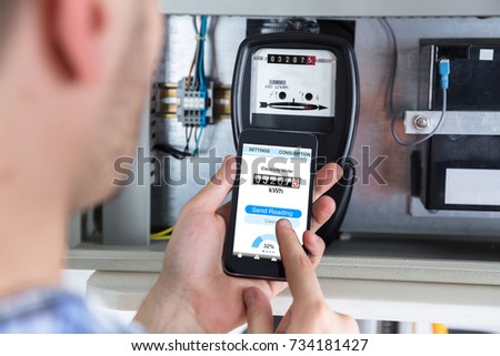 Close-up Of A Man's Hand Holding Mobile Phone Reading Electric Meter