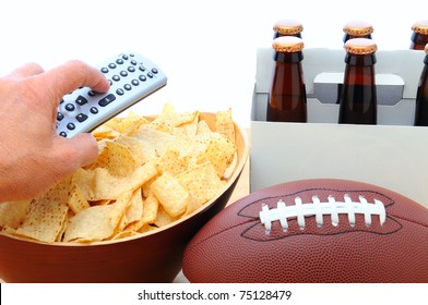 Closeup Of A Man's Hand Holding A TV Remote With A Bowl Of Chips Six Pack Of Beer And Football Isolated On White. Horizontal Format. Great For Bowl Game Projects.