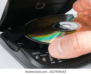 Close-up of a man's hand inserting a CD into a portable CD player.