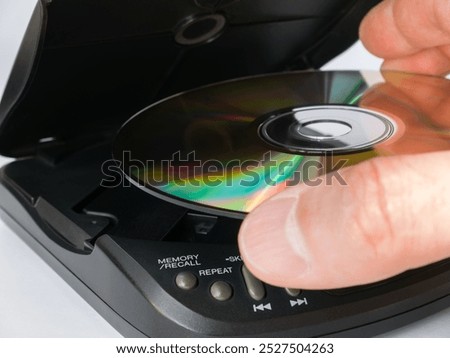 Close-up of a man's hand inserting a CD into a portable CD player.
