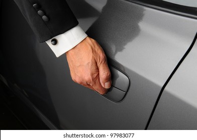 Closeup Of A Mans Hand On The Latch Of A Car Door. The Valet Is Wearing A Tuxedo.