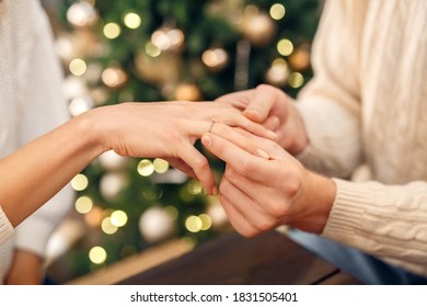 Close-up of mans hand putting engagement ring on womans finger during Christmas or New year celebration with garlands and decorated tree at background at home, selective focus. Proposal, engagement - Powered by Shutterstock