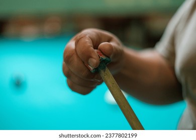 Close-up. A man's hand rubs the tip of a billiard cue with chalk for a more accurate shot. A man prepares to play billiards by rubbing his cue with chalk to prevent it from slipping.