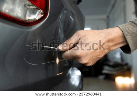 Close-up of a man's hand with a screwdriver scratching the body of a car, damaging someone else's property.