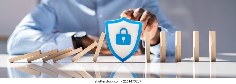Close-up Of A Man's Hand With Shield Security Icon Stopping Dominoes From Falling