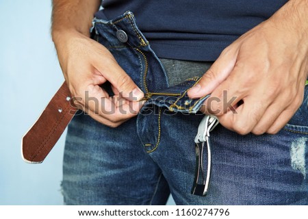 Close-up Of A Man's Hand Unzipping The Blue Jeans. unbuttoned blue pants