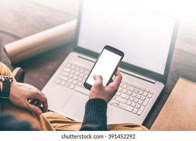 Closeup of man's hand using smartphone with laptop on background