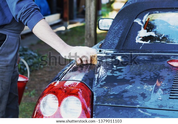 Closeup man\'s hand is washing a car. Hand holds\
sponge to wash car. Cleaning automobile with sponge. Car washing\
and cleaning concept.