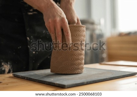 Close-up of a man's hands making a patterned cylinder out of clay. 