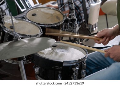 Close-up of a man's hands playing drums. His drumsticks hit with energy, showing the rhythm and motion of live performance. Cymbals and drumheads are slightly blurred, indicating movement. - Powered by Shutterstock