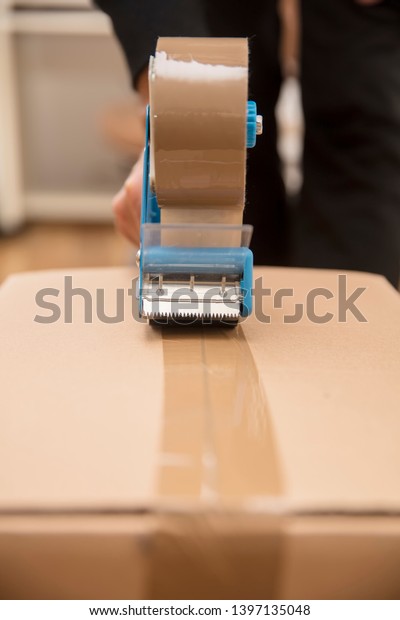 Closeup of the mans hands using a tape dispenser to\
seal a shipping box