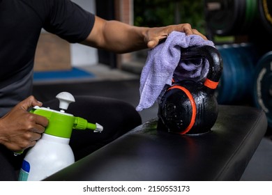 Close-up of a man's hands using a wet wipe and a bottle of disinfectant to clean a kettlebell at the gym. Concept disinfection, cleaning, anti-bacterial - Powered by Shutterstock