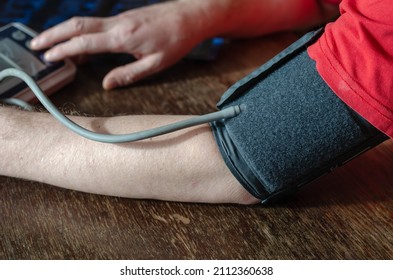 Close-up Of A Man's Shoulder With A Blood Pressure Cuff On. Adult Male Presses Button To Turn On Digital Blood Pressure Monitor. Measuring Blood Pressure At Home. Selective Focus.