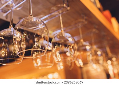 Closeup many upside down empty clear transparent crystal upturned wine glasses hanging in straight rows on brown wooden shelf, rack, showcase, stainless steel railing in bar, cabinet