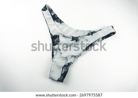 Close-up of a marble-patterned bikini bottom laid flat on a white background, showcasing its sleek design, smooth fabric texture, and monochrome abstract print style.